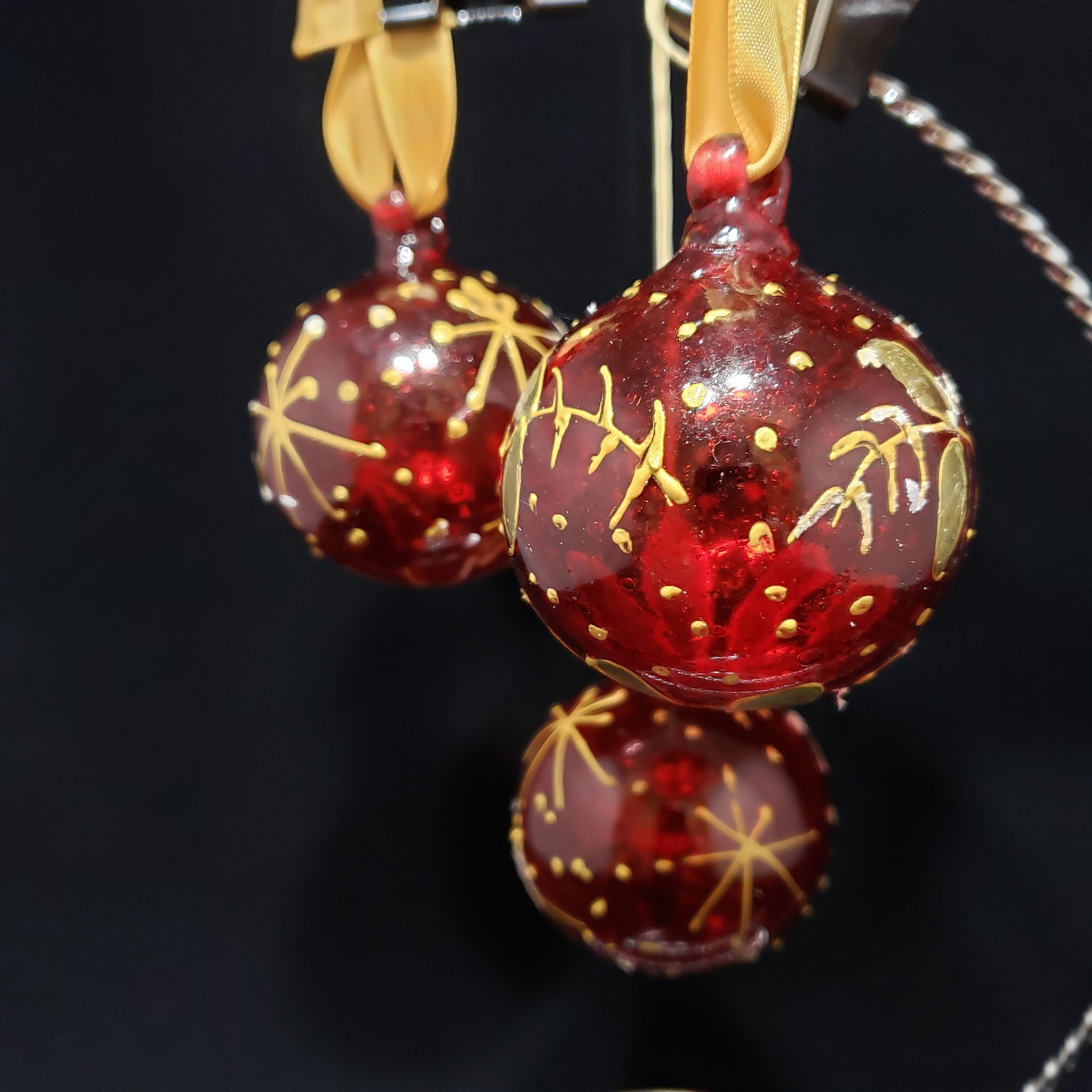 Two red handblown glass Christmas ornaments with gold details and a gold satin ribbon for hanging.